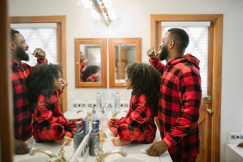 Father and daughter in matching pajamas brushing teeth together in a cozy bathroom.